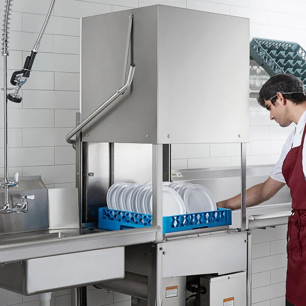 Worker operating a commercial dish machine, illustrating the equipment covered by a dish chemical program.