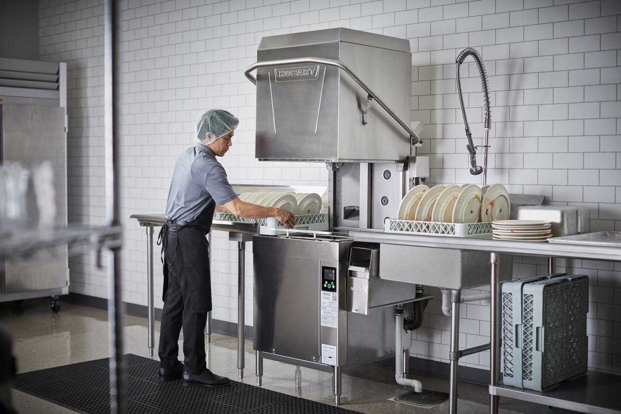 Worker operating a commercial dishwasher, illustrating the equipment covered by dish chemical and service vendor programs.