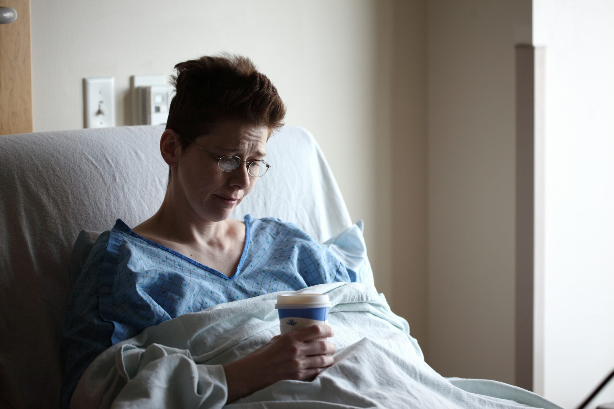Patient in a healthcare facility holding a hot beverage while resting in bed.