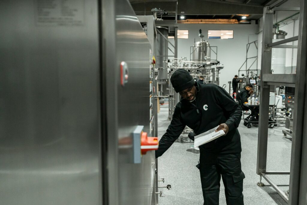 Technician inspecting stainless steel beverage production equipment while holding a service checklist