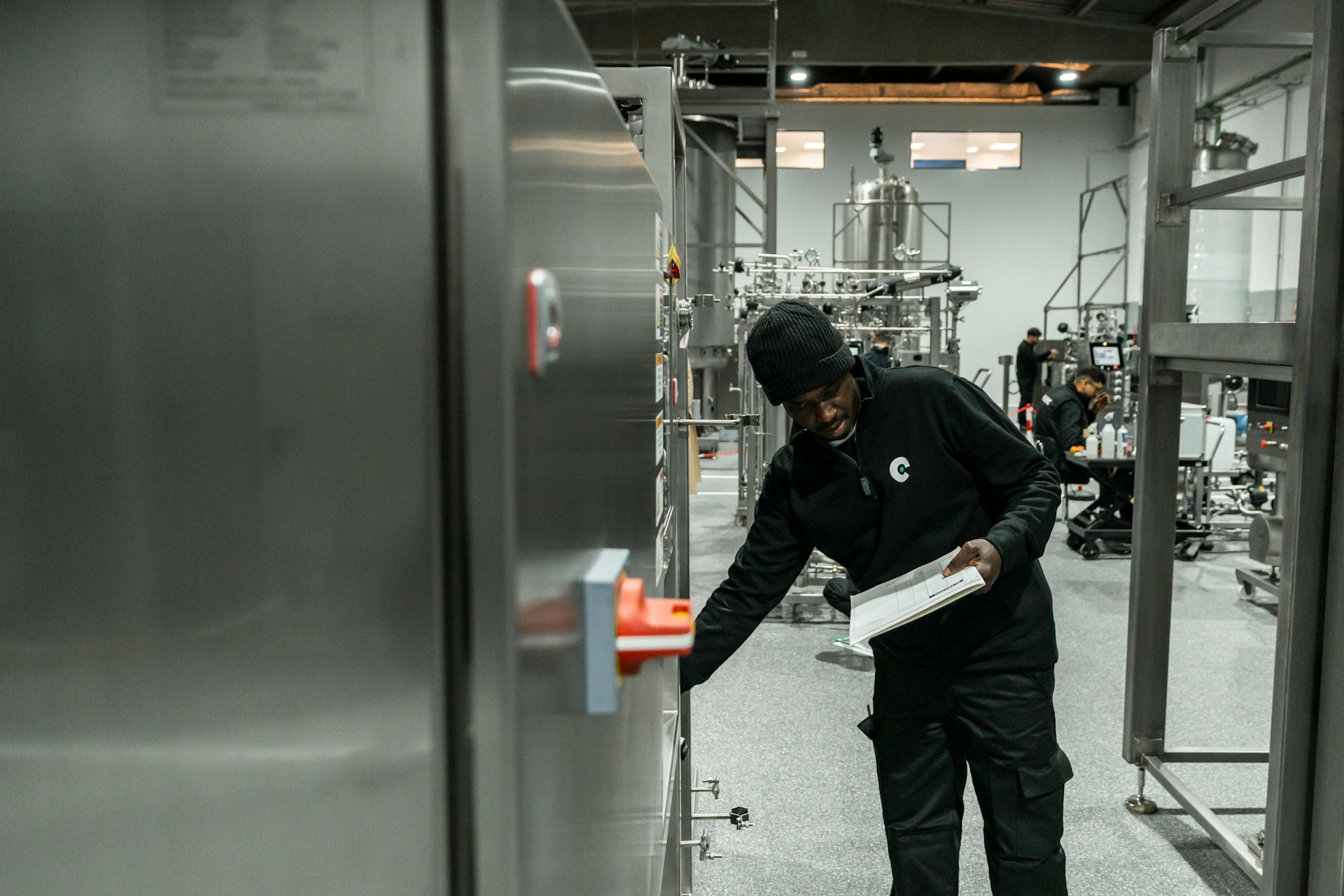 Technician inspecting stainless steel beverage production equipment while holding a service checklist