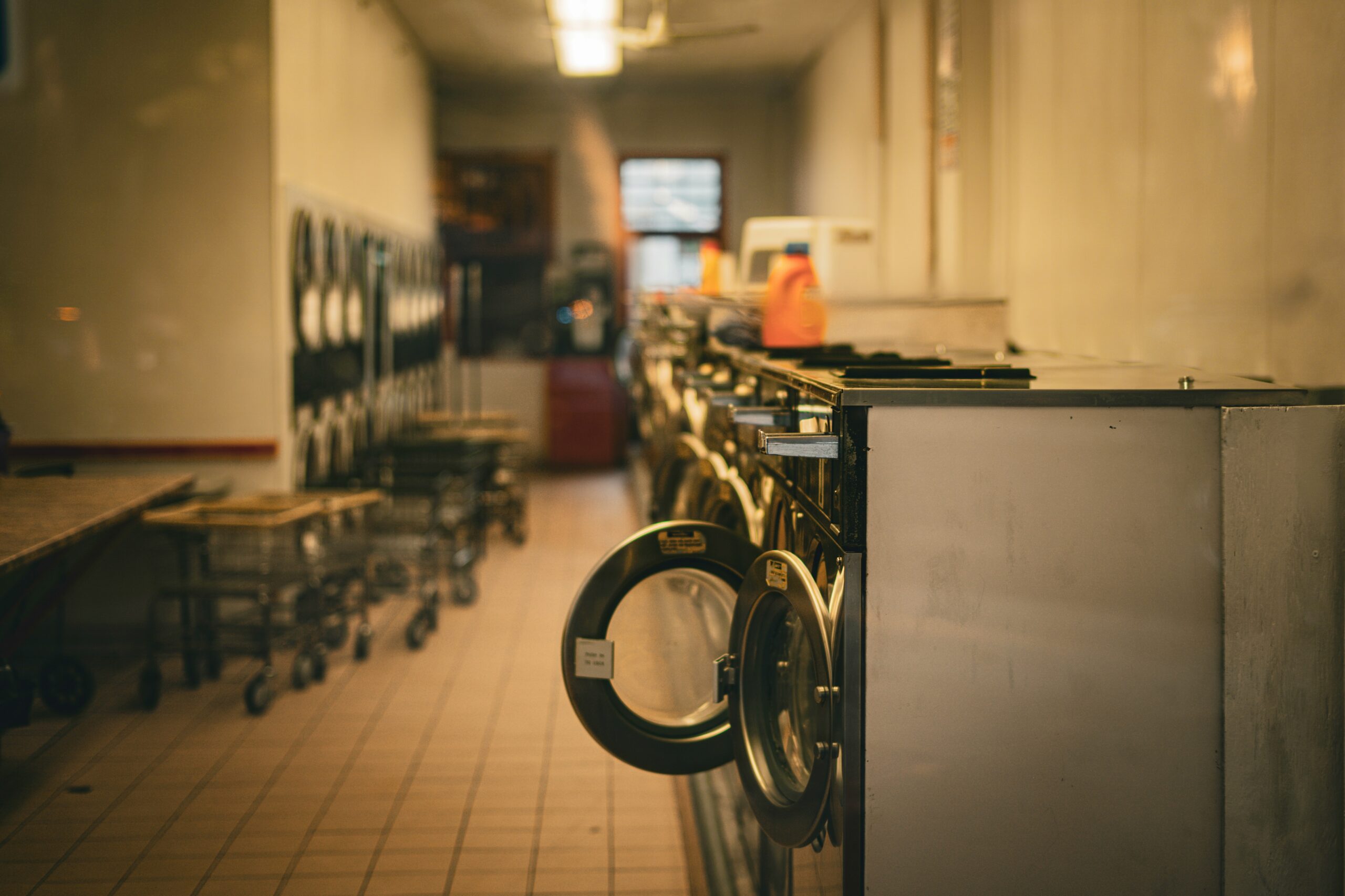 Row of commercial laundry machines with detergent, representing the laundry chemical programs covered alongside dish machine service in vendor comparisons.