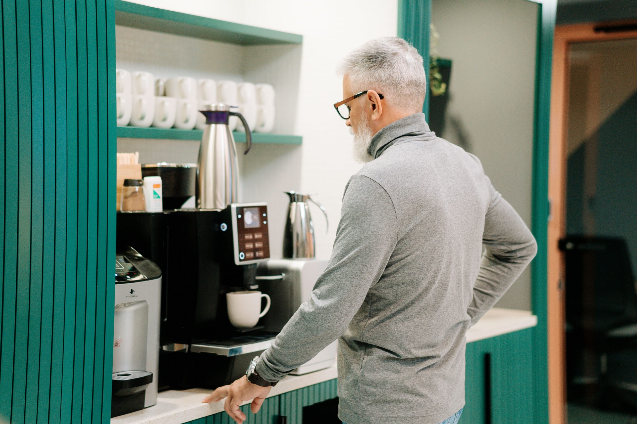 Office manager inspecting a commercial office coffee machine and brewing station in a bright breakroom