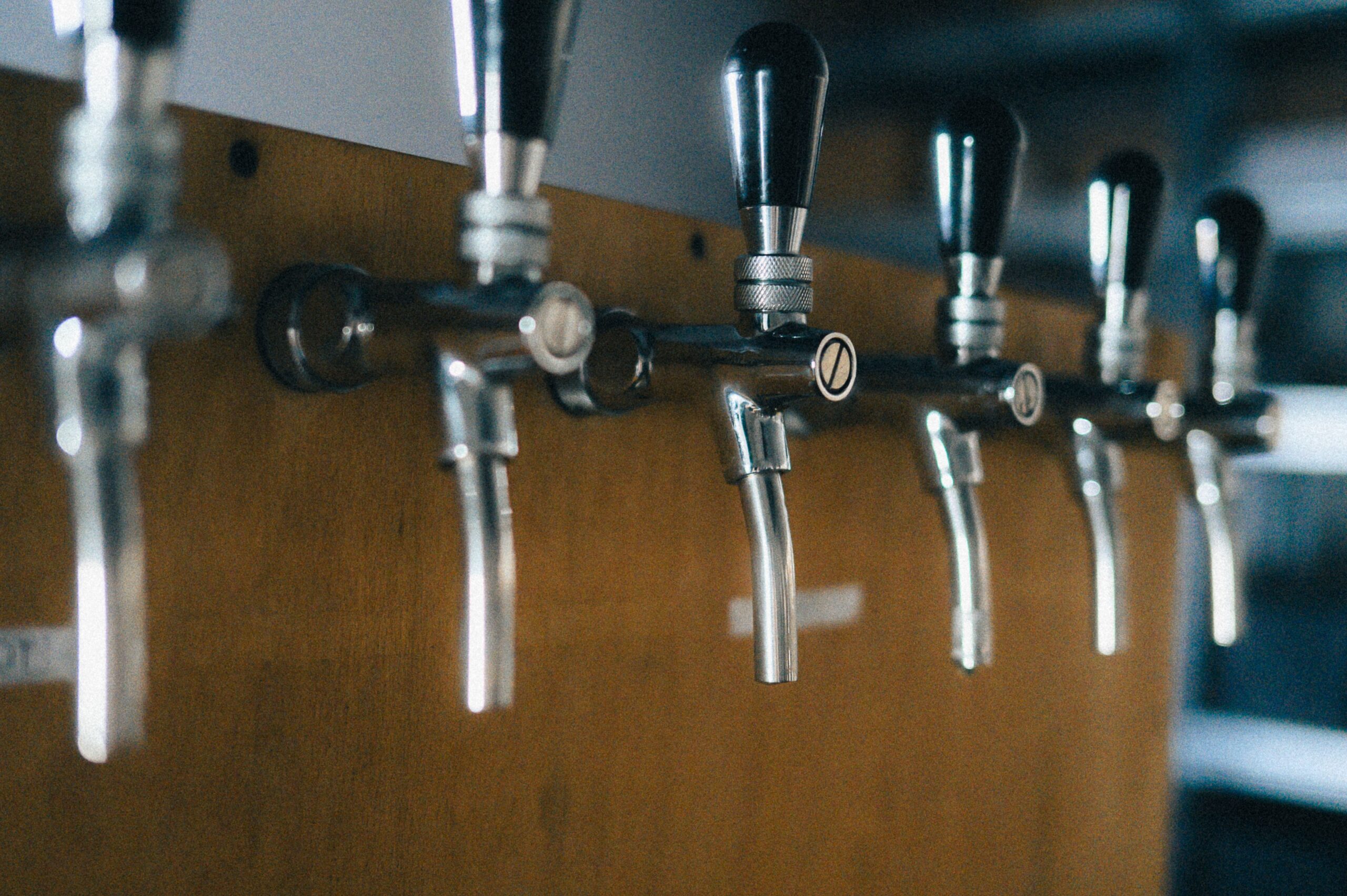 Row of stainless steel tap faucets on a wooden bar tower, where beer line cleaning matters most