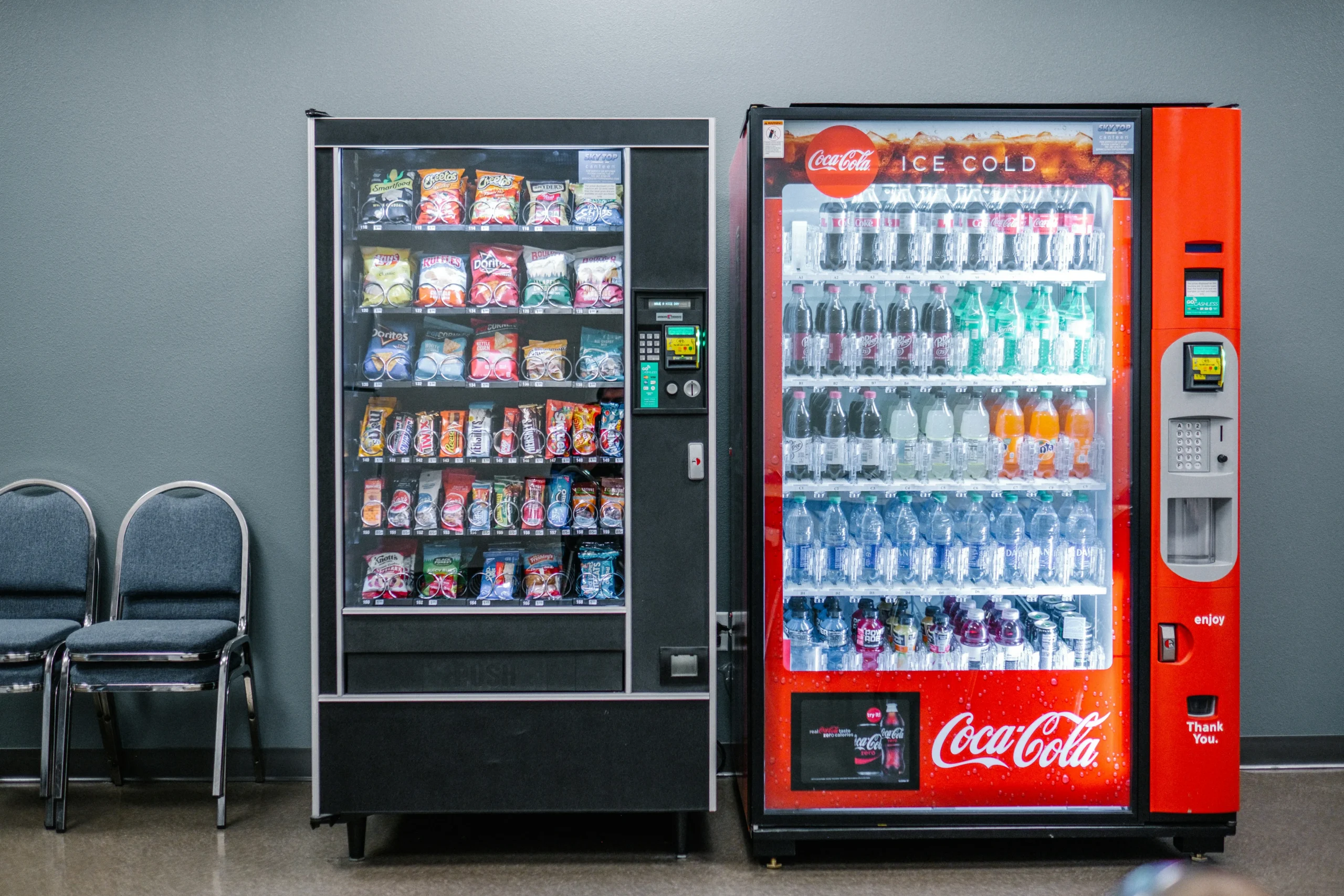 Traditional vending machines stocked with packaged snacks and cold bottled beverages in a workplace or commercial setting.